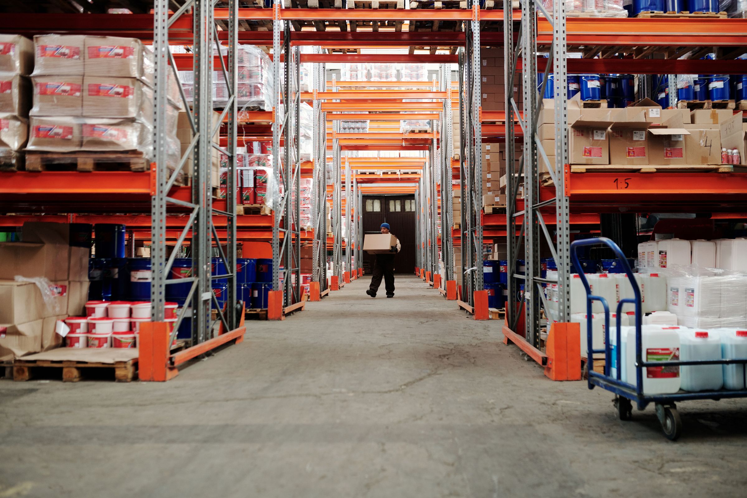 Warehouse worker carrying a carton down a stocked aisle