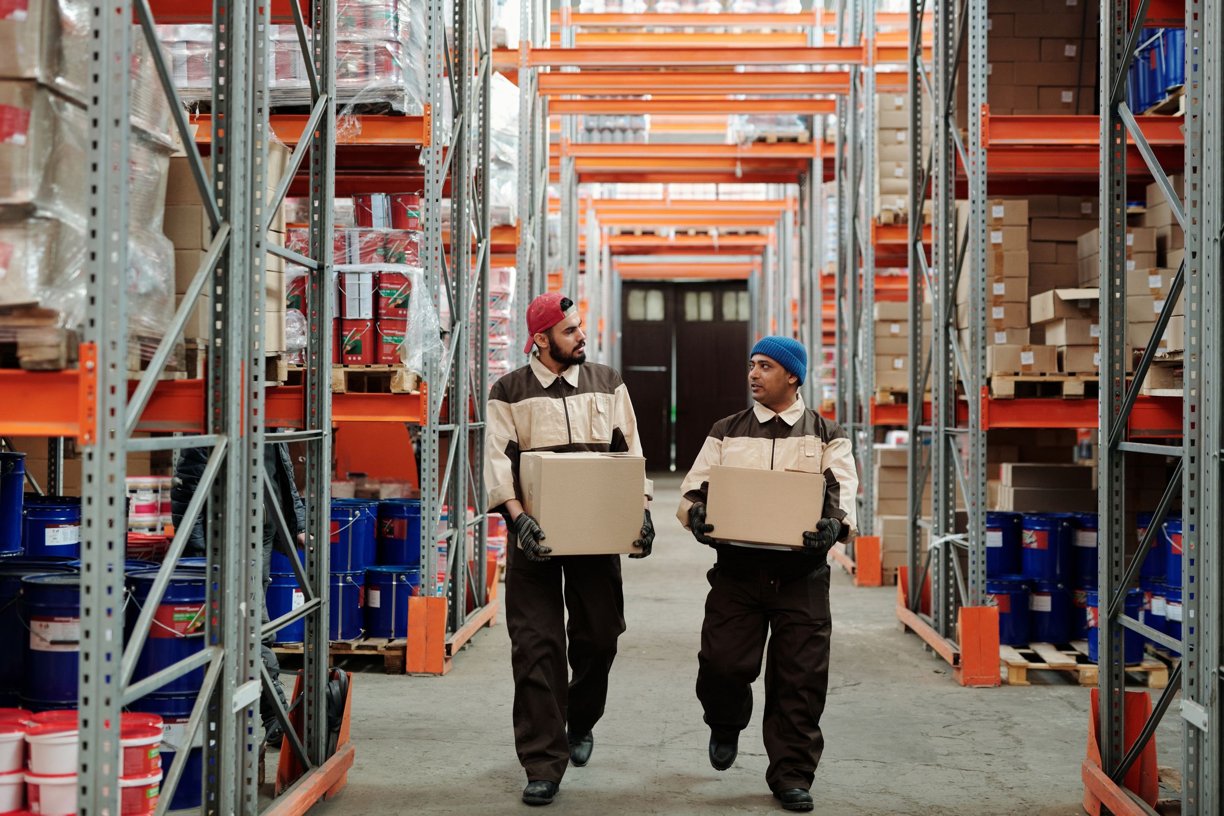 Two warehouse workers carrying cartons down an aisle